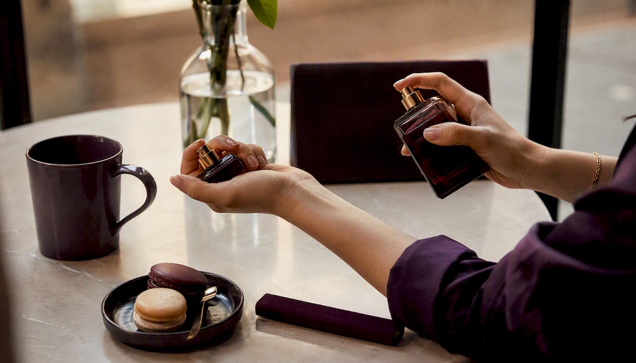 Hands comparing two fragrance sprays on elbow