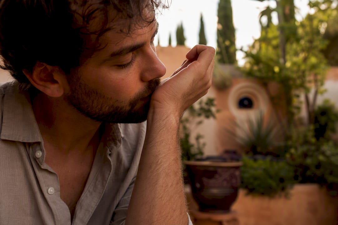 Hombre aplicándose perfume en la muñeca y oliéndolo al aire libre