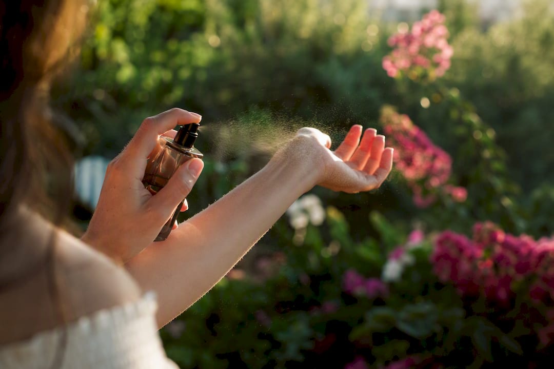 Un geste délicat : vaporiser son parfum sur le poignet, baigné par la lumière du soleil.