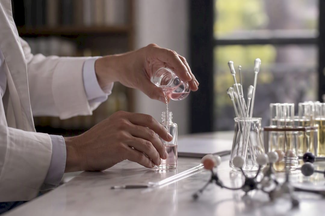 Mains versant un liquide aromatique dans des fioles en verre de laboratoire