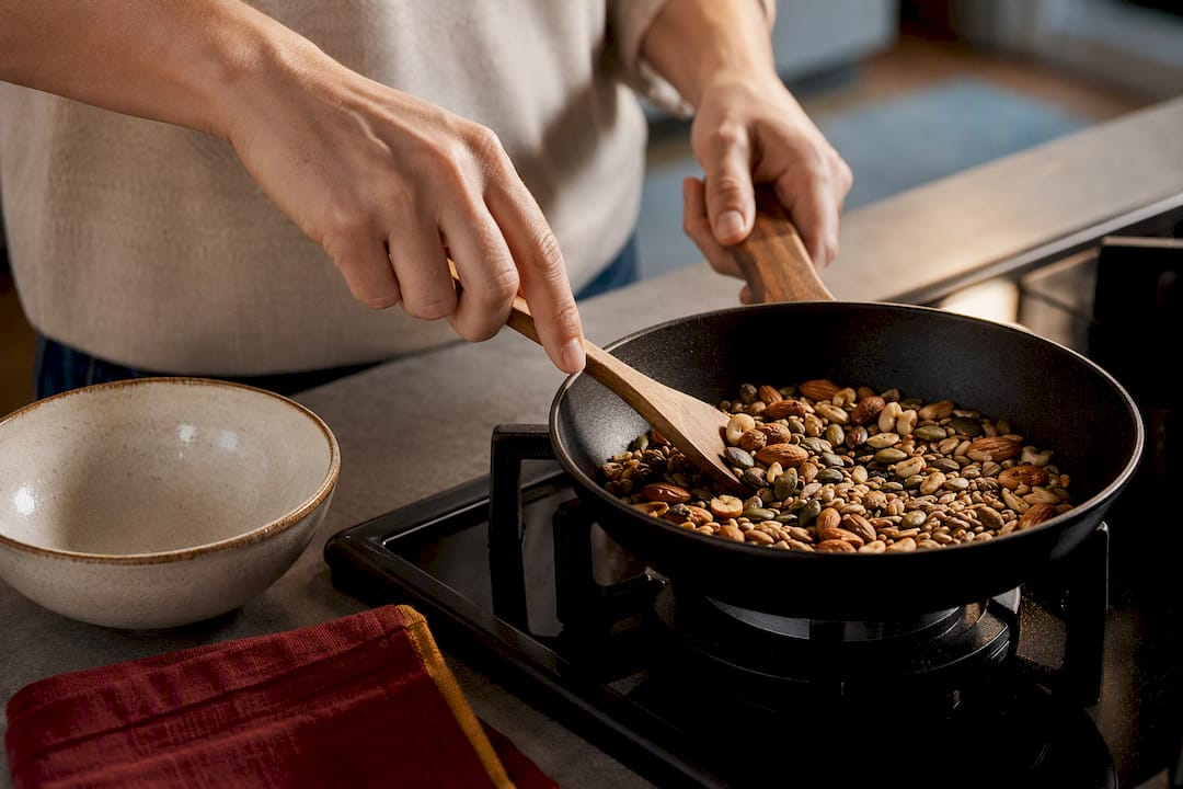 Hands toasting nuts and seeds in skillet