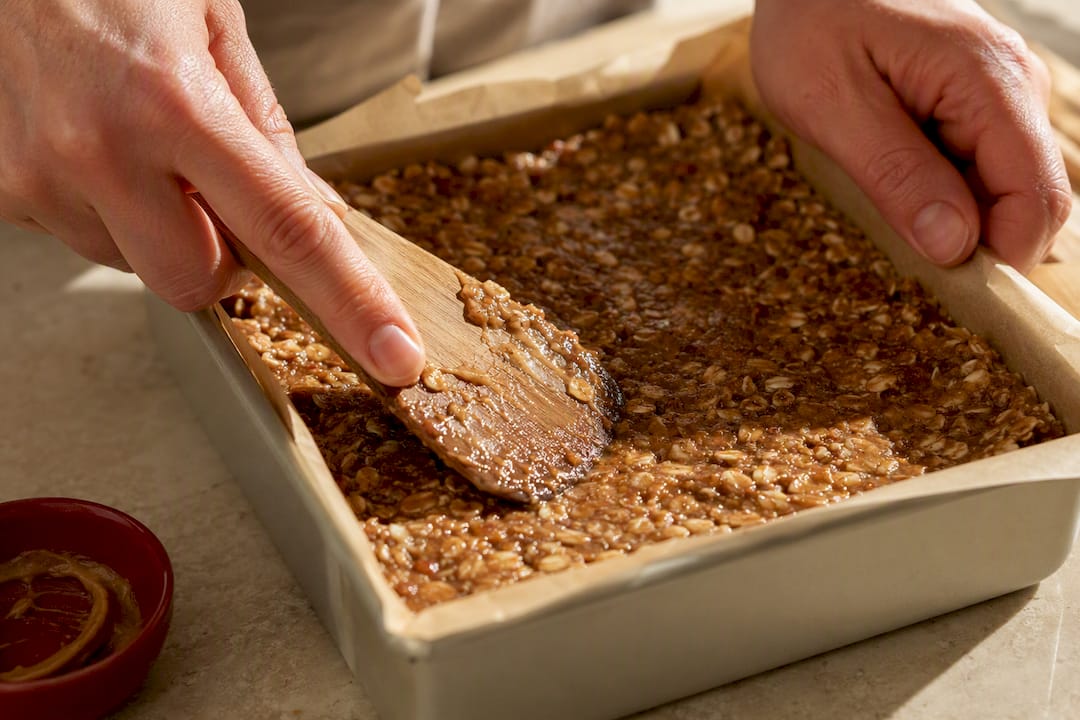 Hands pressing oat mixture into pan