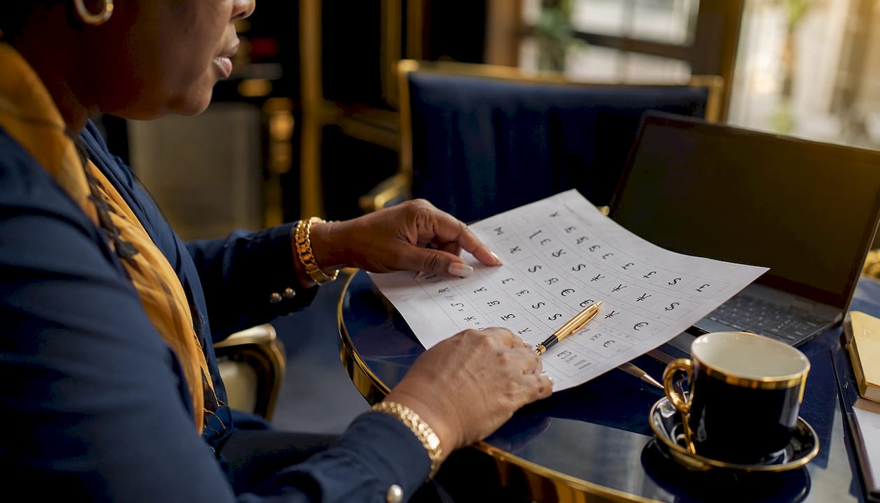 Hands comparing currency symbols chart on desk