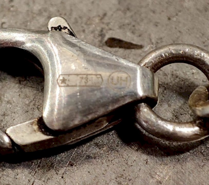 Mani che esaminano il marchio di autenticità di un gioiello in argento con una lente d’ingrandimento.