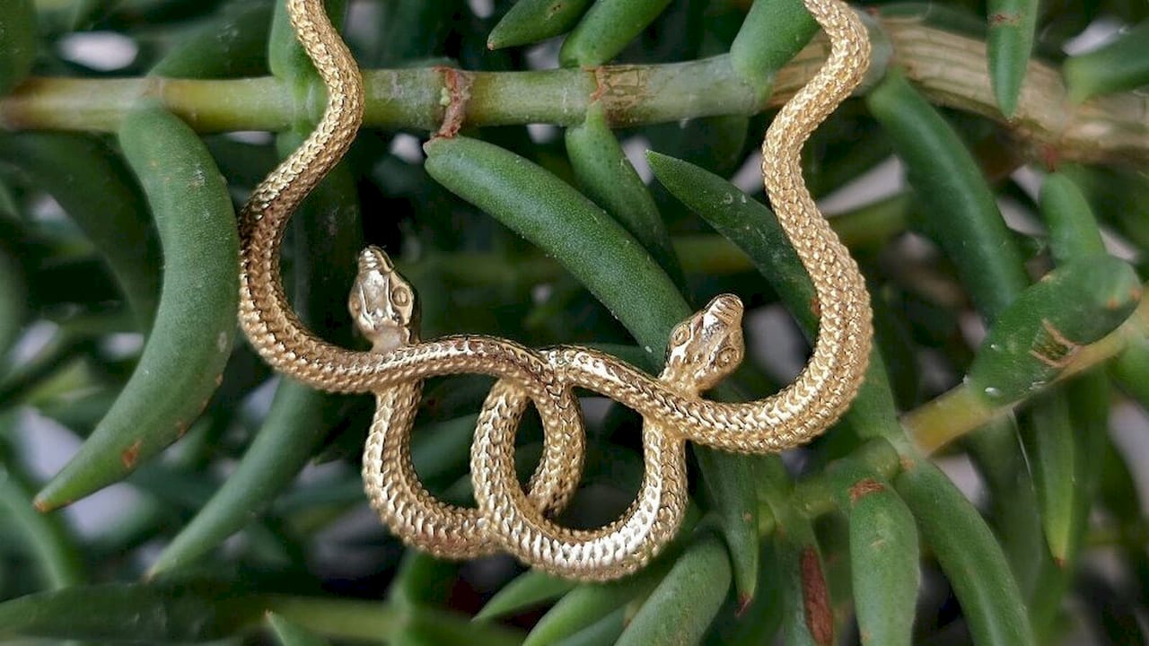Dettaglio di orecchini a cerchio raffiguranti un serpente in ottone, appoggiati su una superficie di legno.