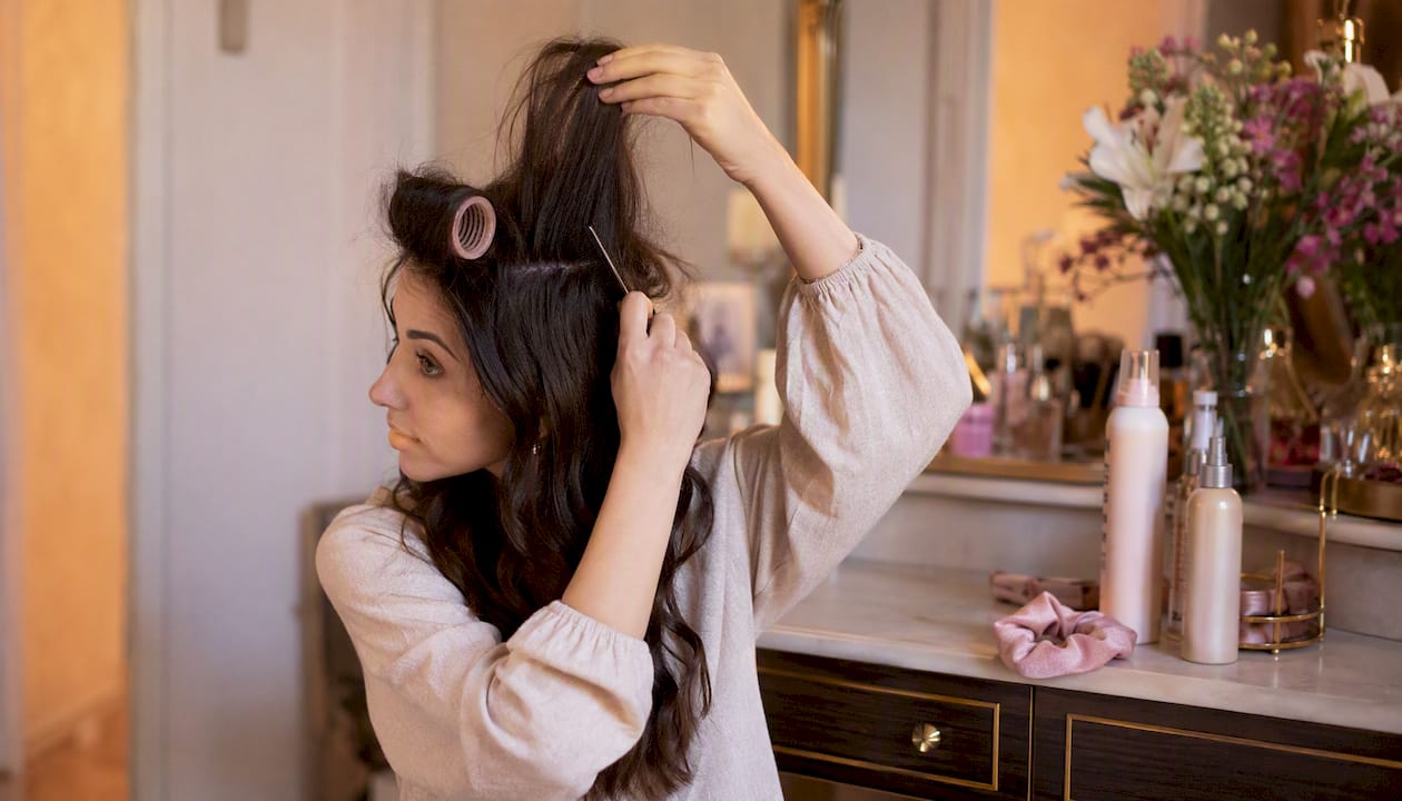 Woman teasing hair with comb and rollers
