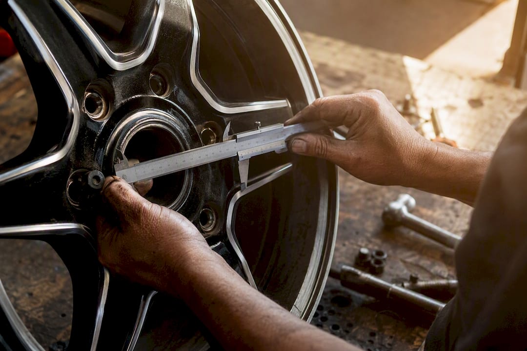 Hands measuring lug holes with caliper on truck wheel