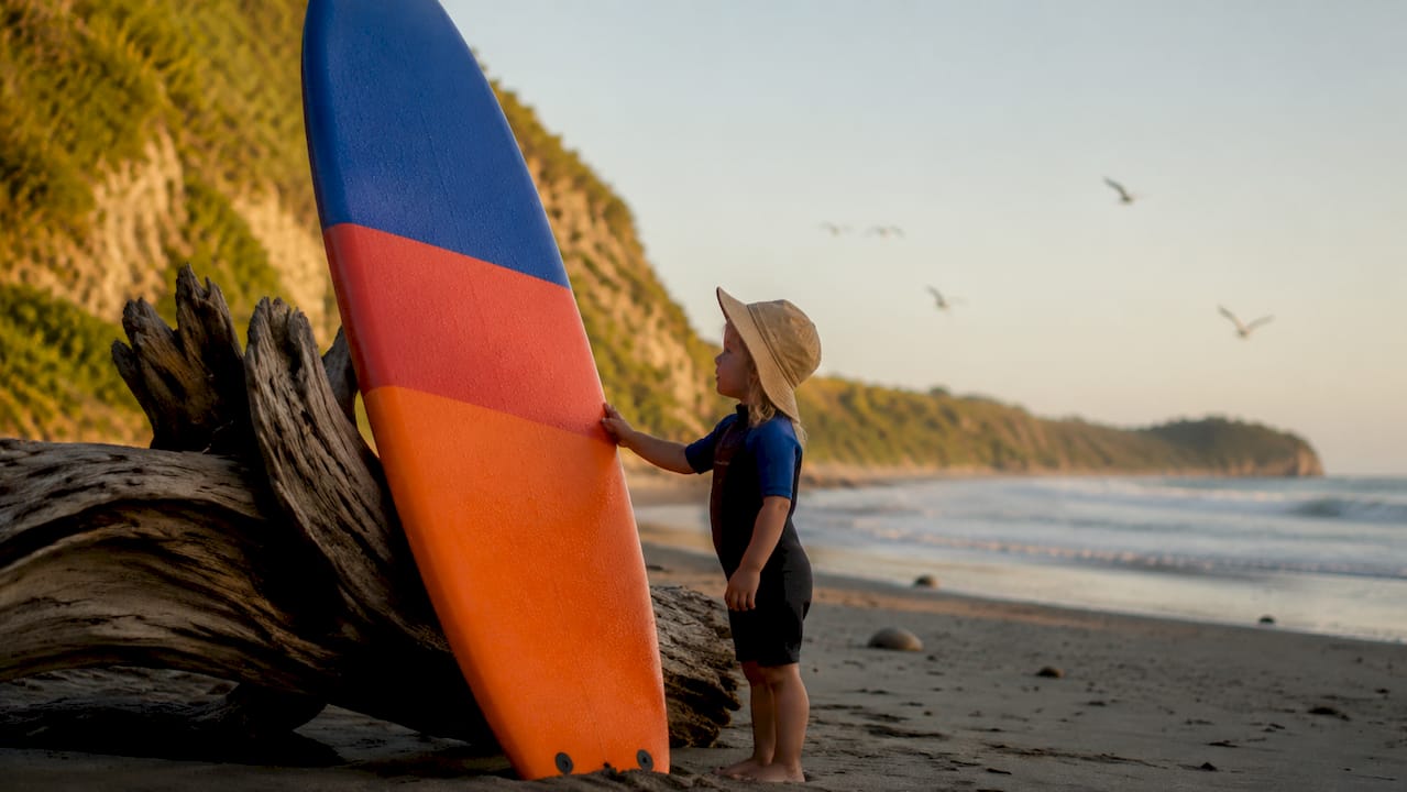 Child hand touching soft-top surfboard on beach