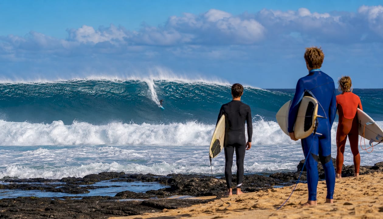 Surfer riding giant North Shore winter wave near rocky coast