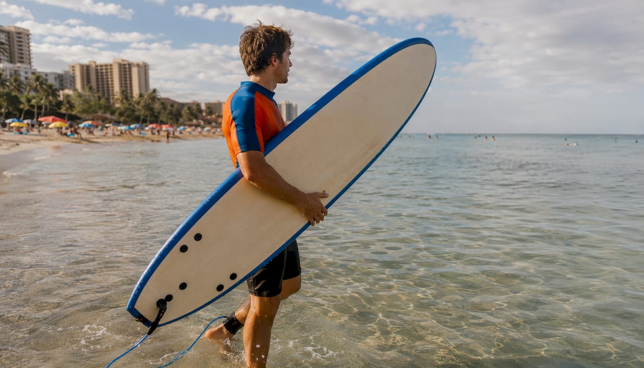 Surfer entering shallow water holding beginner soft-top surfboard