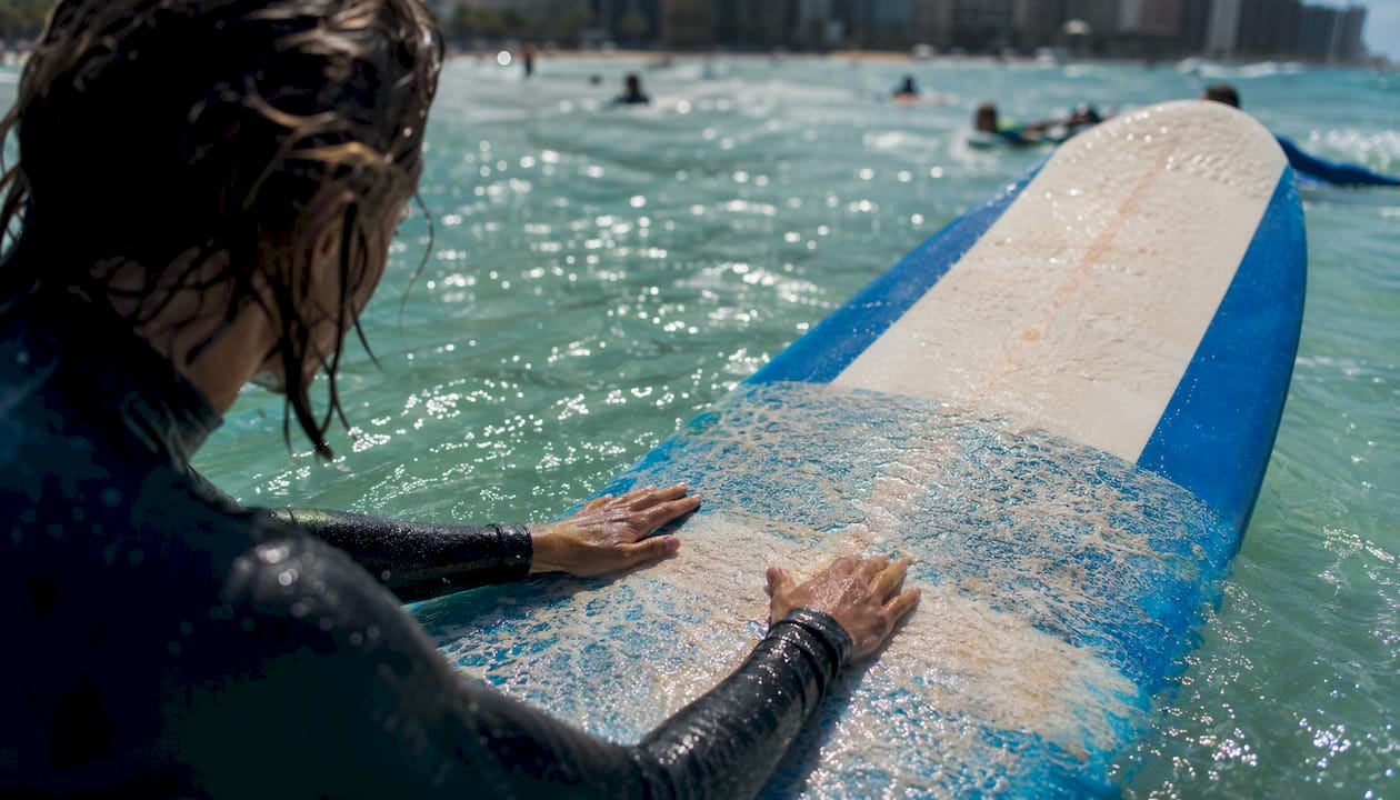 Hands gripping surfboard rail in crowded Waikiki lineup