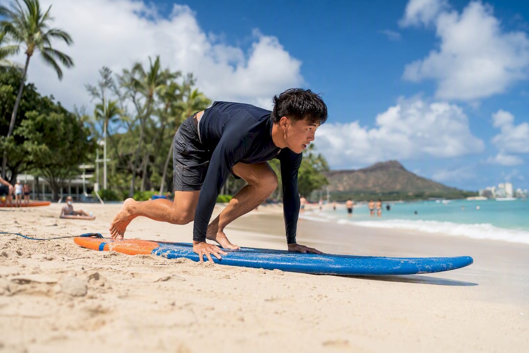 Beginner practicing surf pop-up drill on beach sand