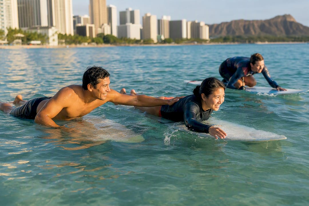 Instructor coaching two students on surfboards in water
