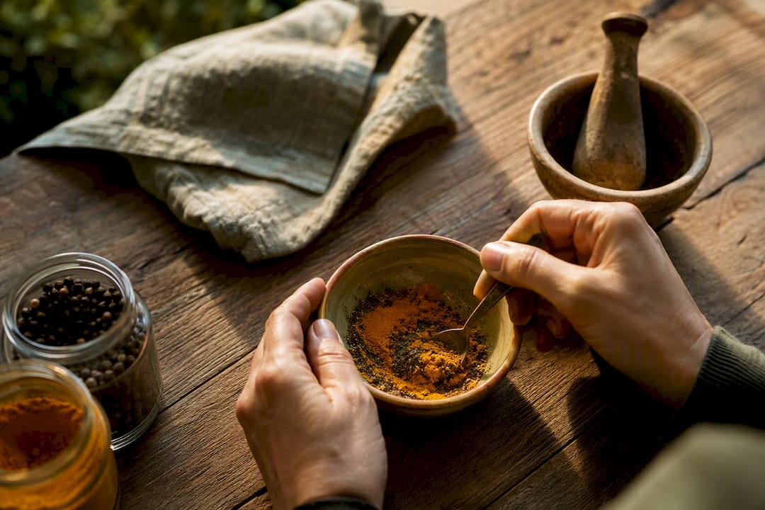 Hands sprinkling black pepper onto turmeric powder