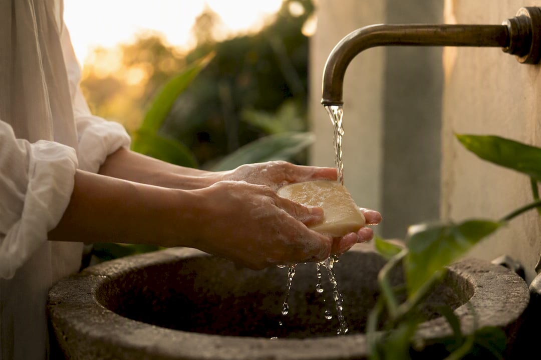Hands applying solid cleansing bar under water