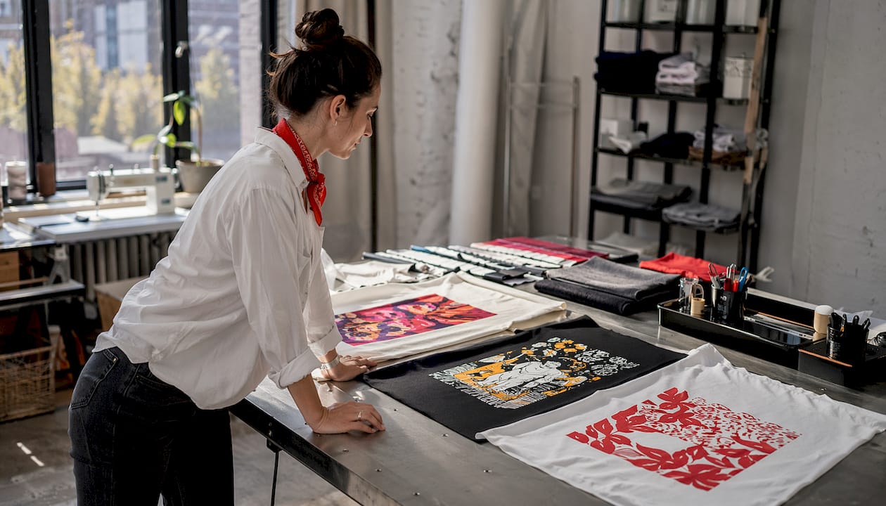 Hands comparing direct to film, screen print, and HTV fabric samples