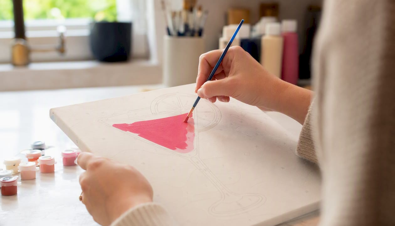 Hands painting a simple martini glass shape on canvas