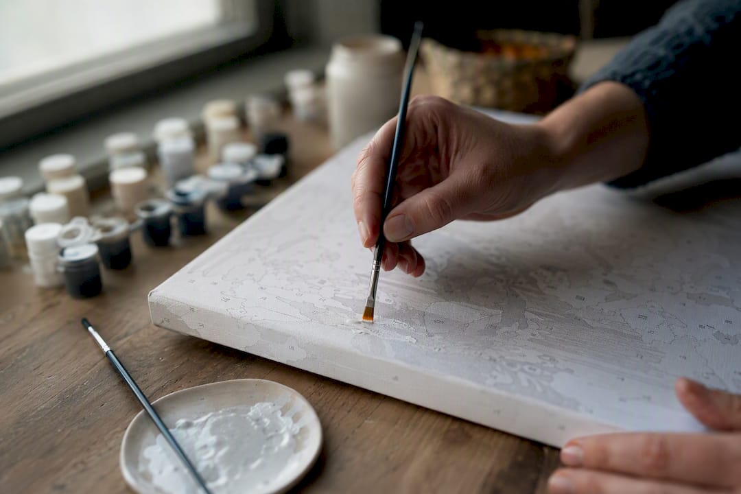 Hands painting thin white coat over canvas numbers