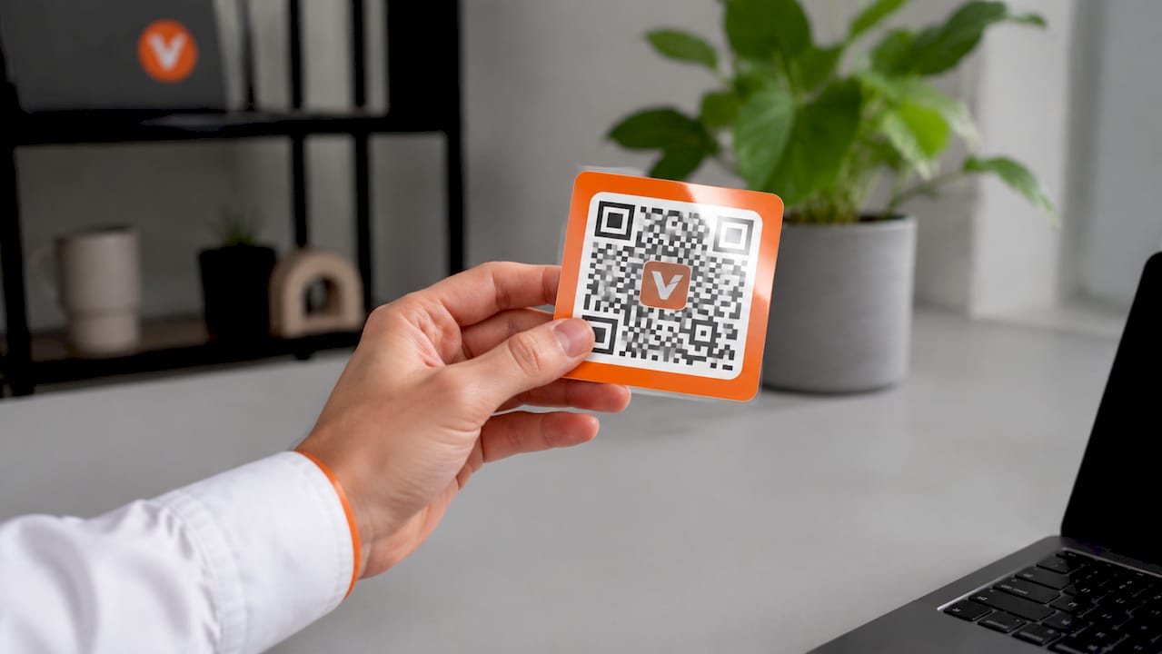 Een hand houdt een gelamineerde sticker met QR-code vast.