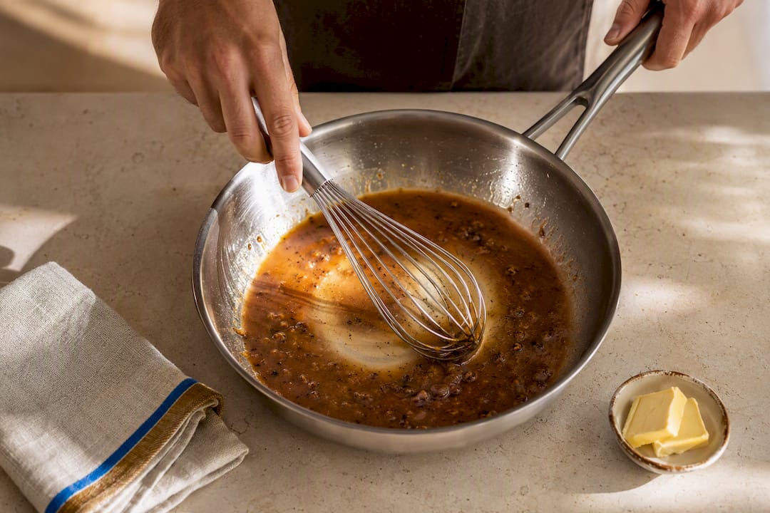 Hands whisking a glossy French pan sauce