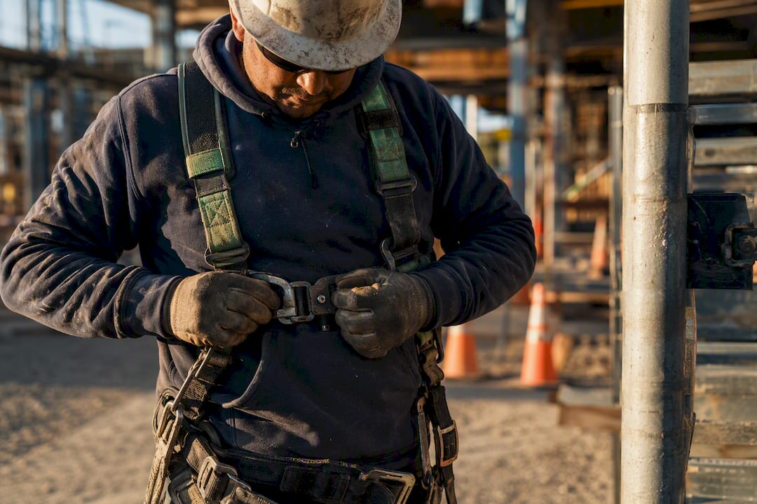 Worker fastening fall protection harness at construction site