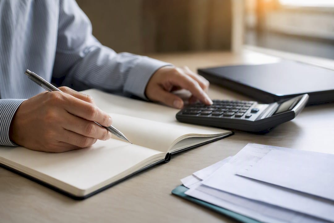 Hands allocating freight costs with calculator and ledger