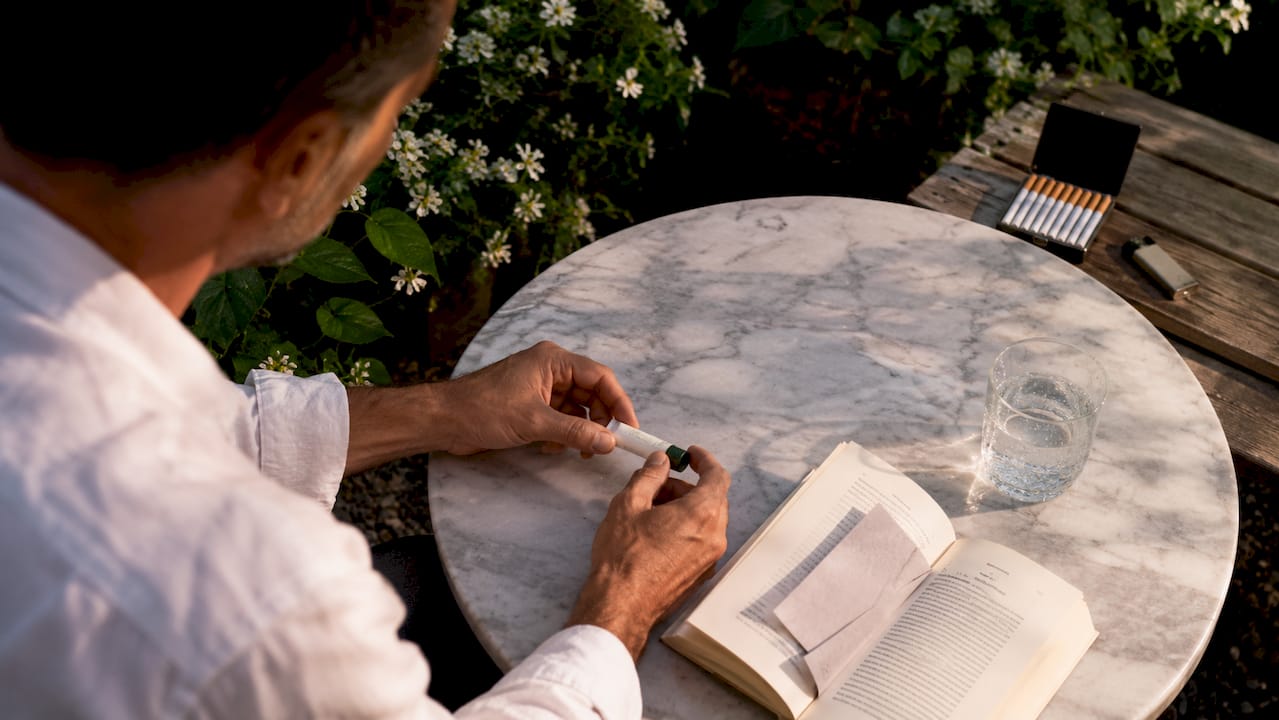 Hands with oral nicotine gel and lit cigarette outdoor scene