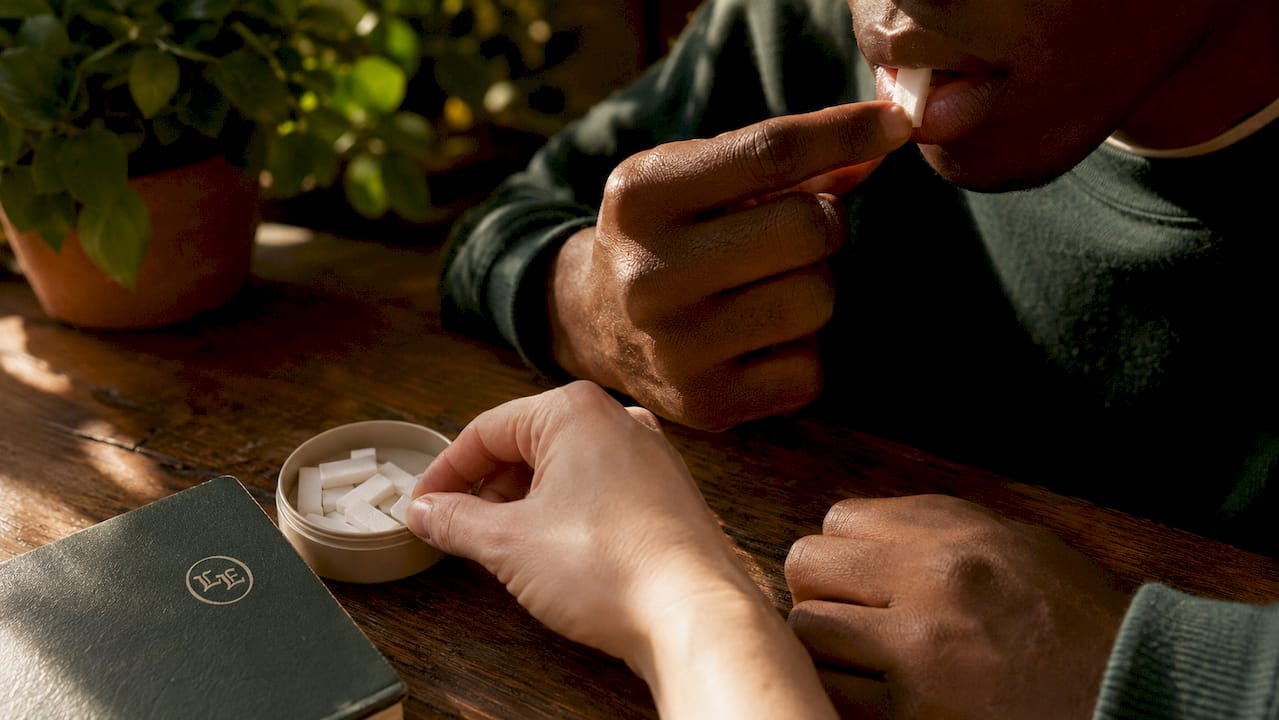 Hands placing nicotine pouch inside mouth