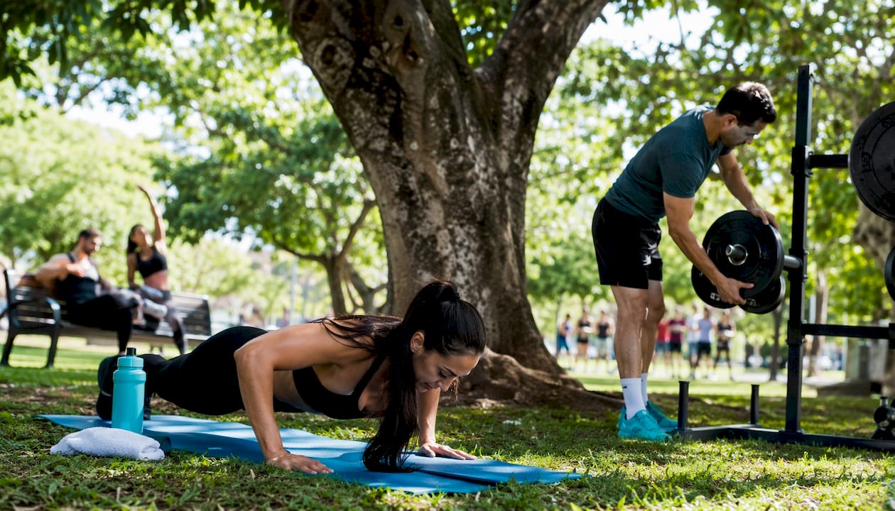 Woman doing push-up beside man adjusting barbell