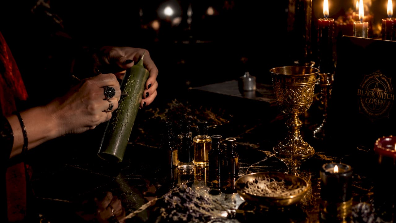 Hands carving ritual candle surrounded by oils and herbs