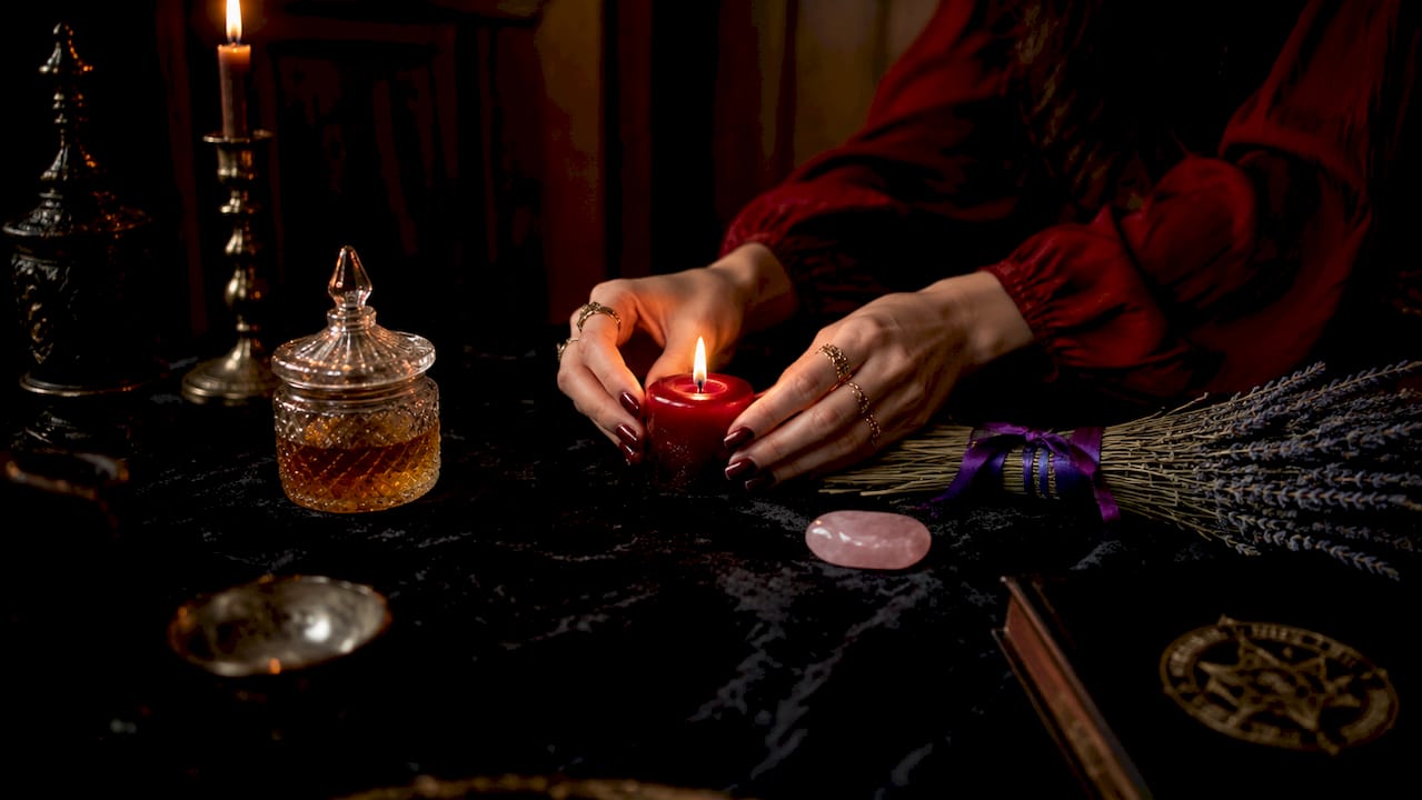 Hands holding red candle over ritual altar