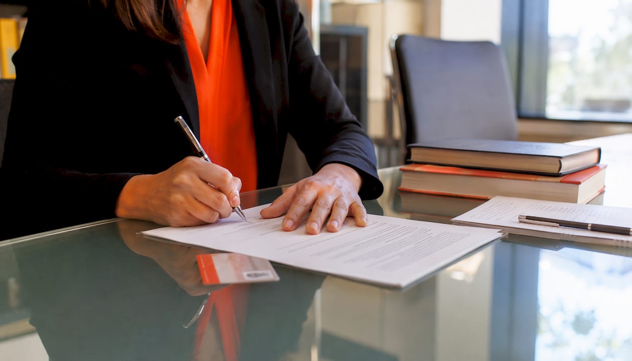 Hands signing certified translation papers with NAATI card