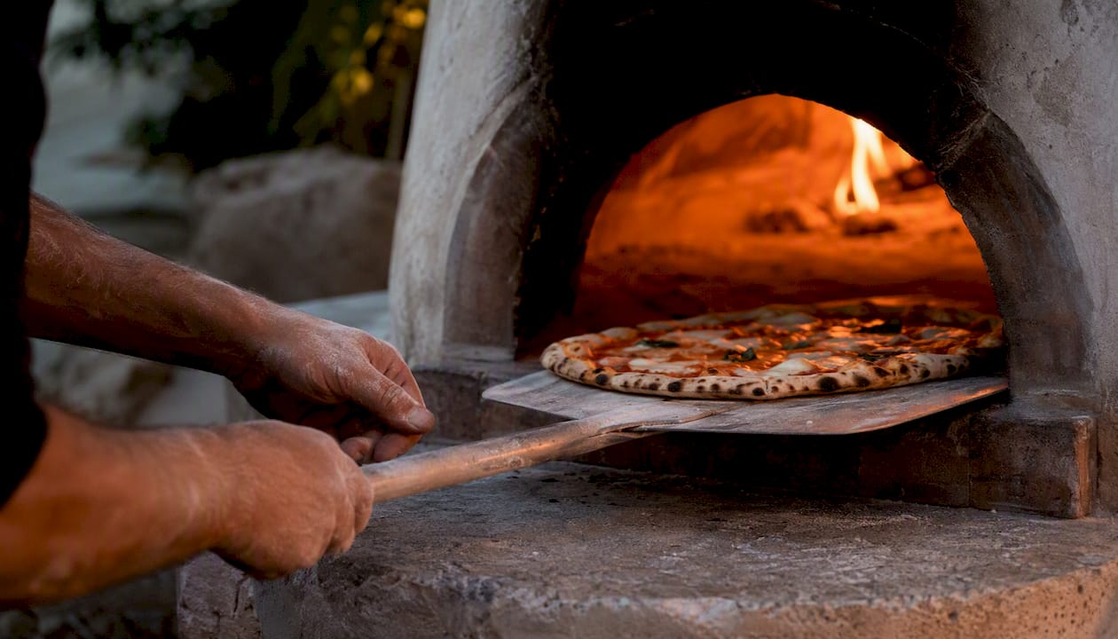Hands placing pizza in wood oven