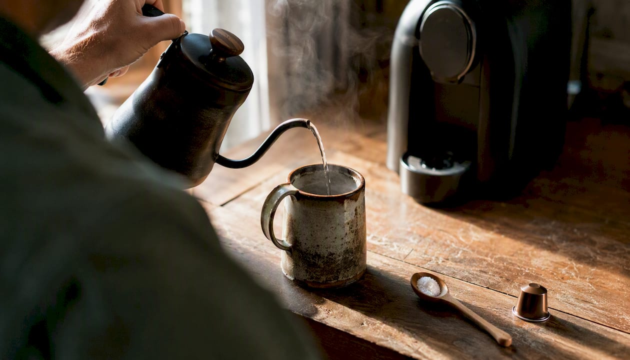 Pouring hot water into mug to preheat before coffee pod brewing