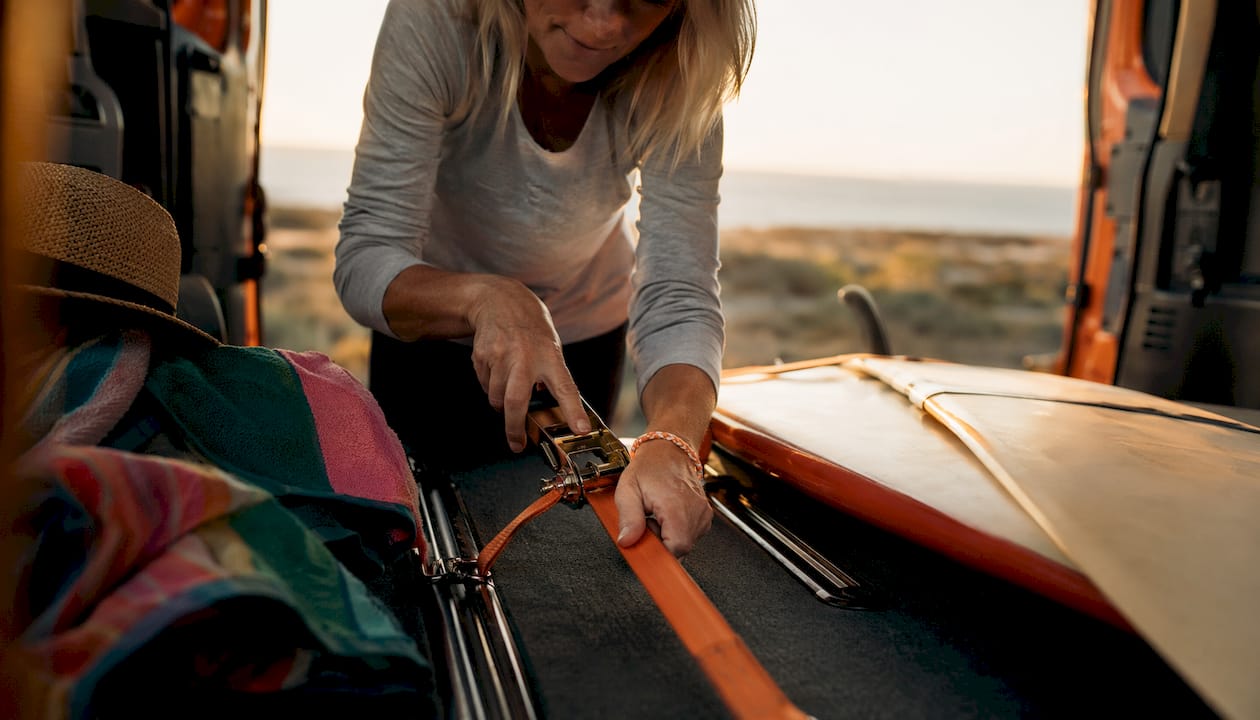 Person securing surfboard with straps inside van