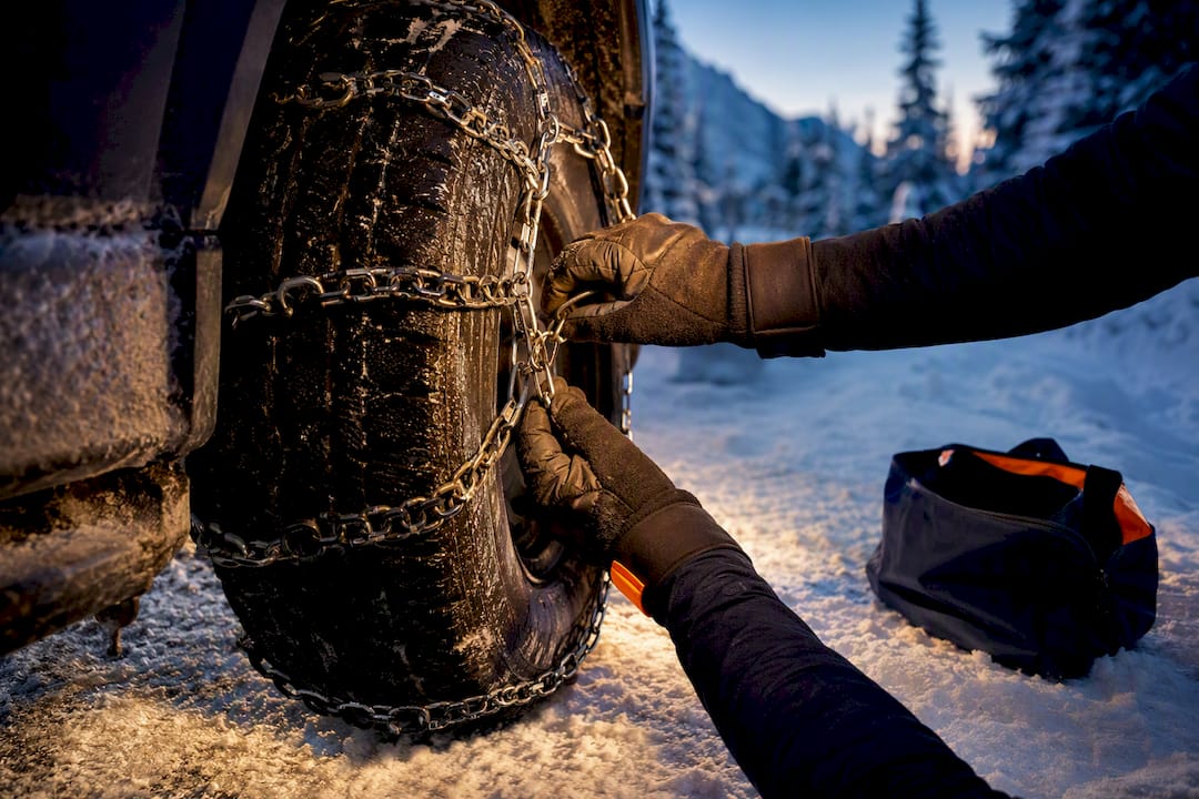 Hands fitting chains to tire on snowy road