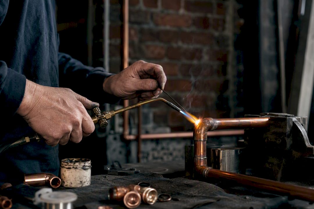 Hands soldering copper pipe joint with torch