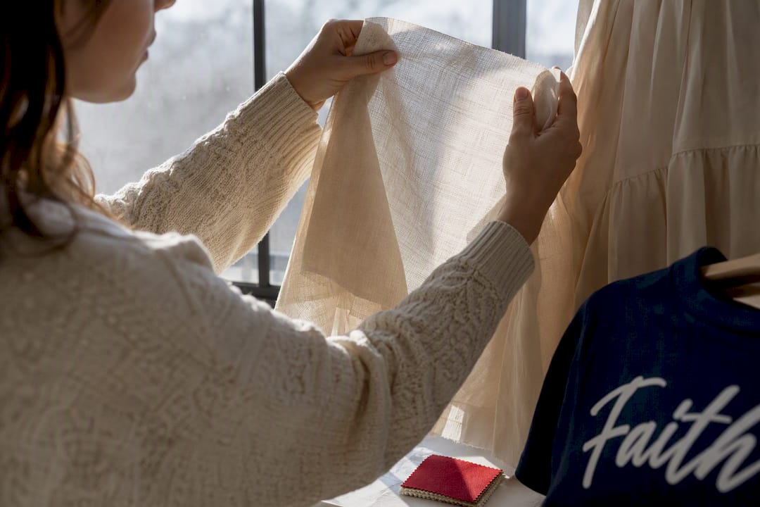 Hands testing fabric opacity beside window
