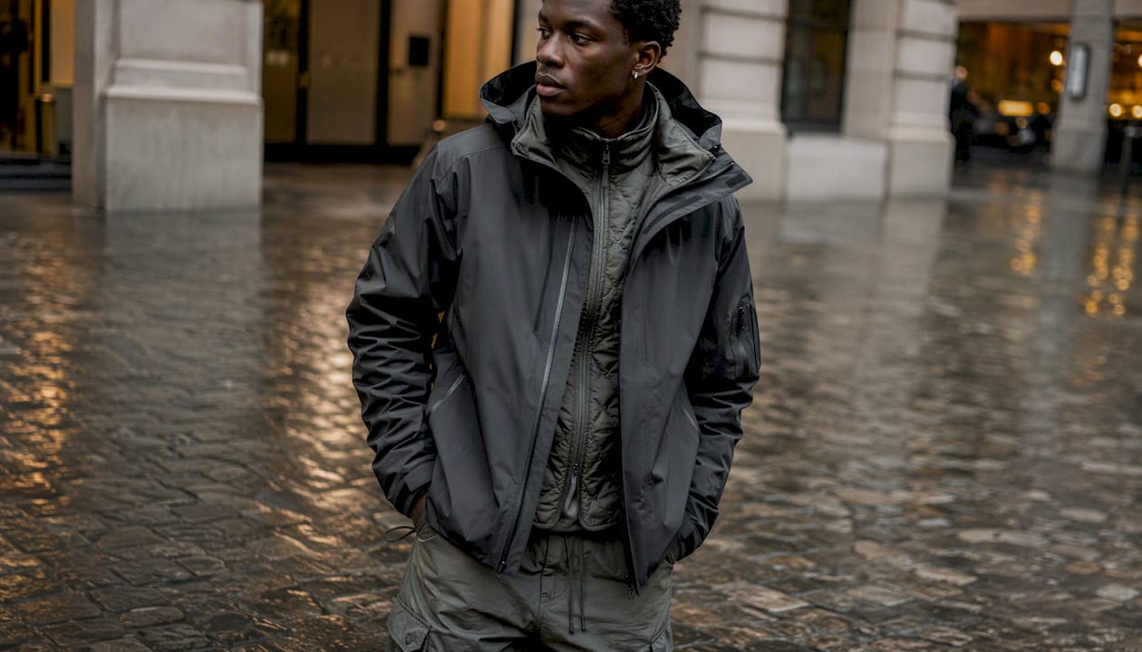 Techwear layering with shell jacket and quilted vest on wet street