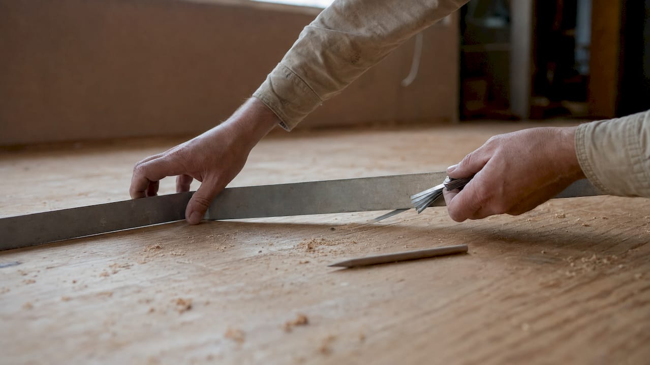 Hands measuring subfloor flatness with tools