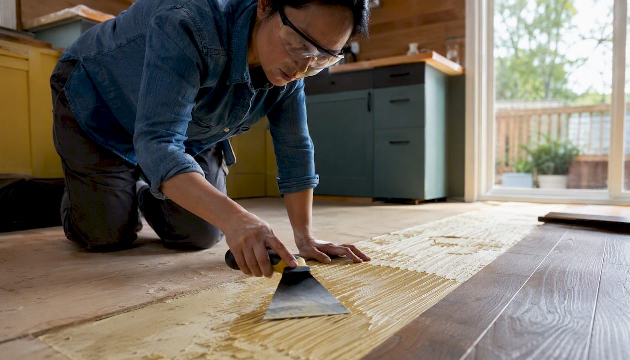 Installer spreading adhesive with trowel on subfloor