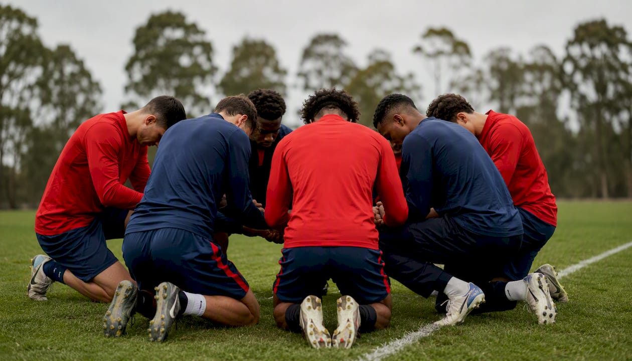 Soccer team kneeling in prayer circle on field