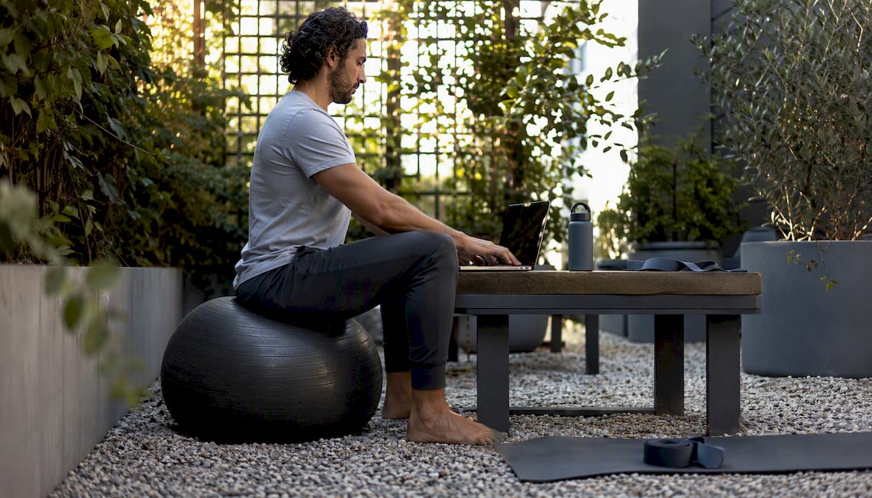 Tall person sitting on large exercise ball at desk