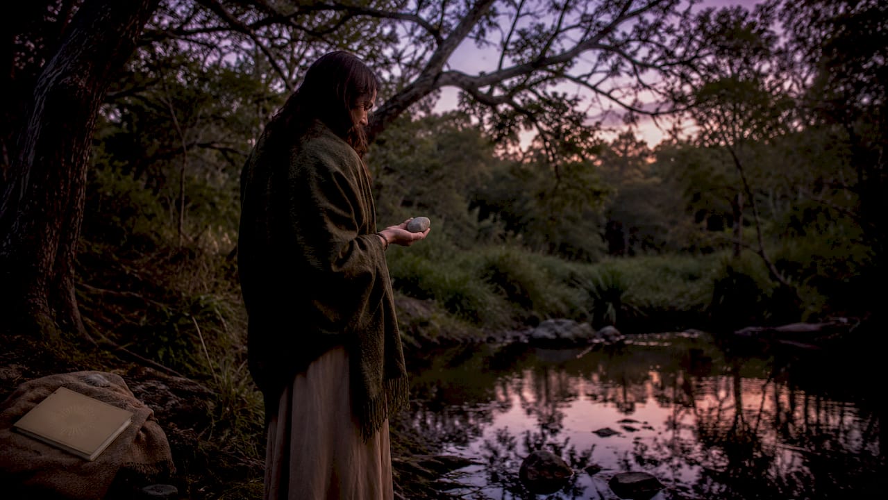 Figure holding crystal by peaceful forest stream