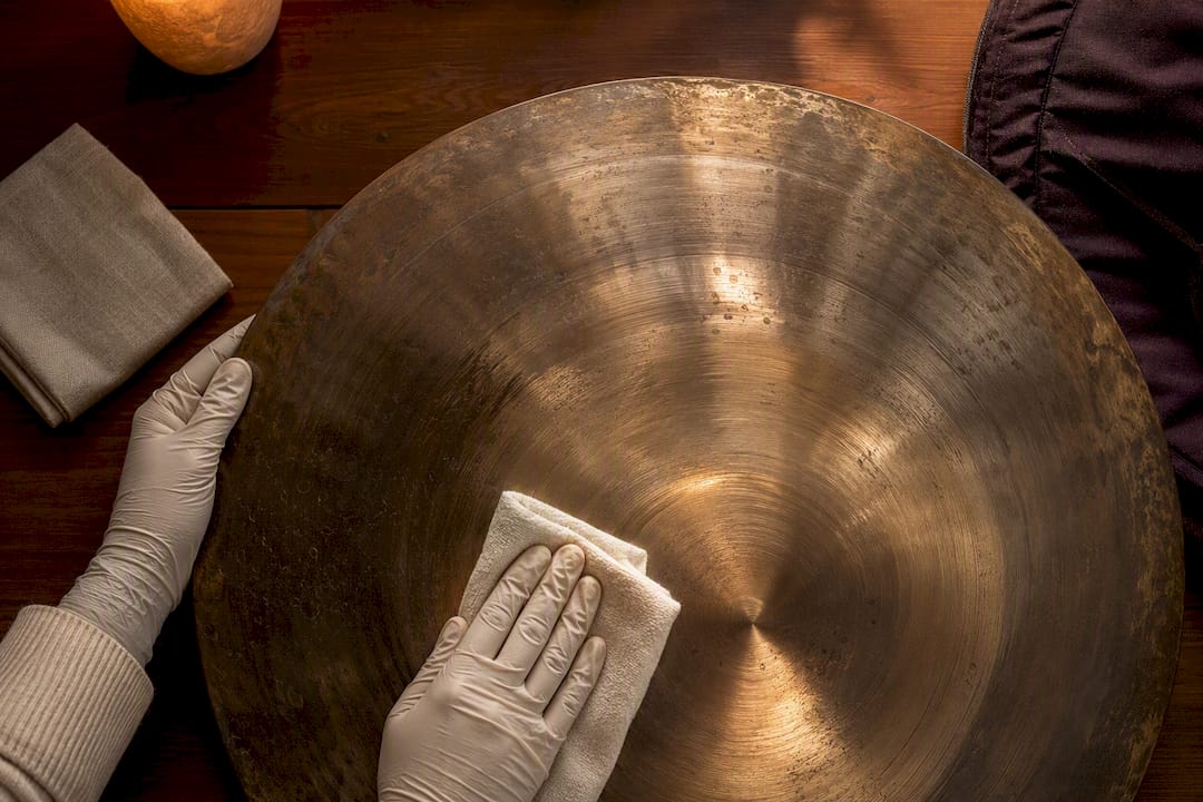Gloved hands carefully wiping bronze gong