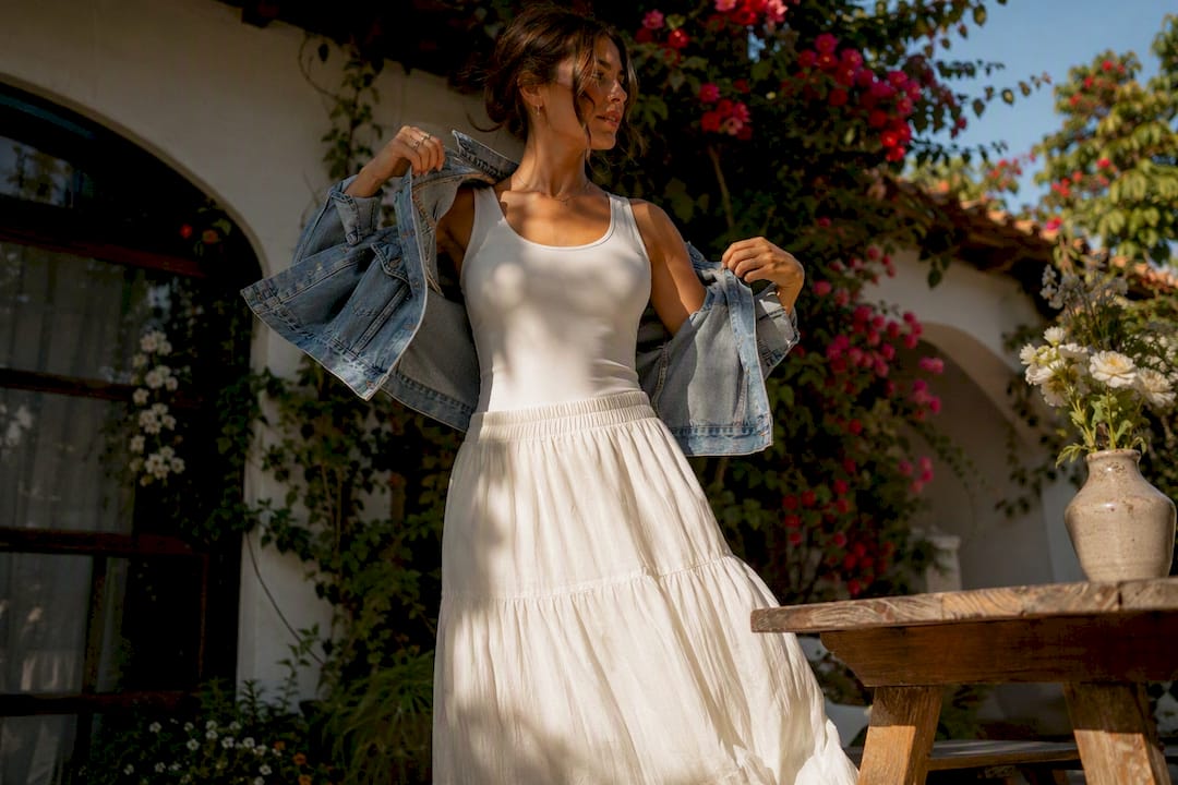 Woman layering denim jacket over cotton skirt outfit outdoors