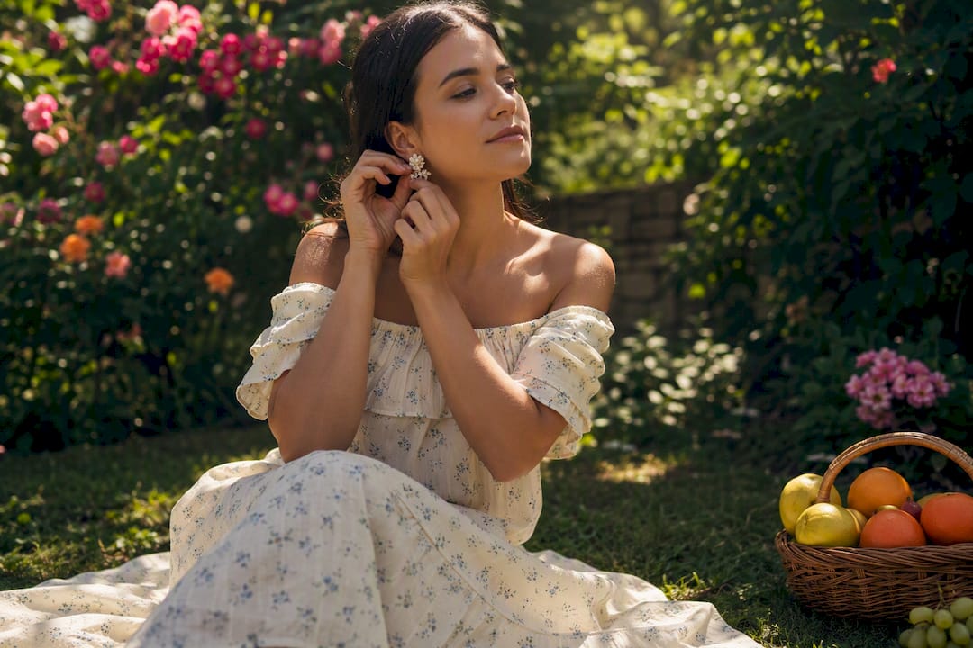 Woman adjusting earrings in off-shoulder cotton dress