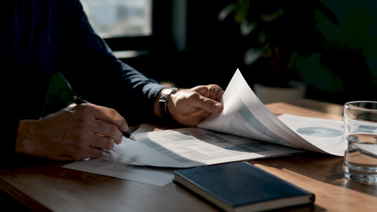 Des mains font défiler l’écran d’une tablette au milieu de dossiers et de papiers de bureau.