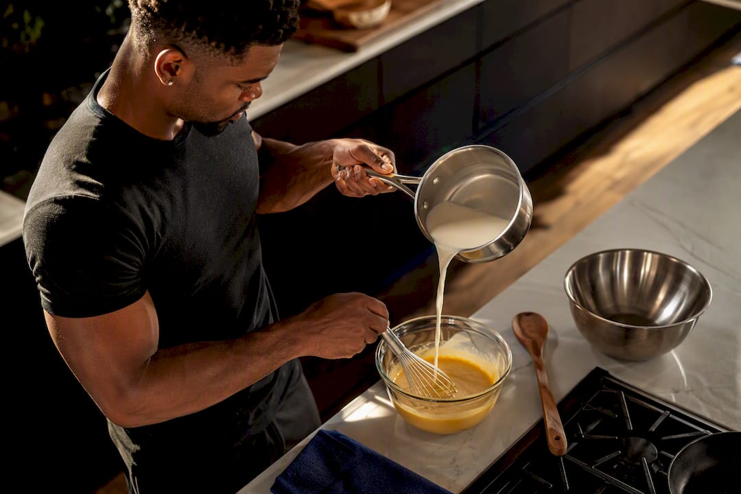 Black man tempering milk into egg yolks