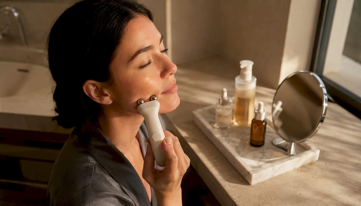 Una donna applica un dispositivo a microcorrente sul viso per prendersi cura della sua pelle.
